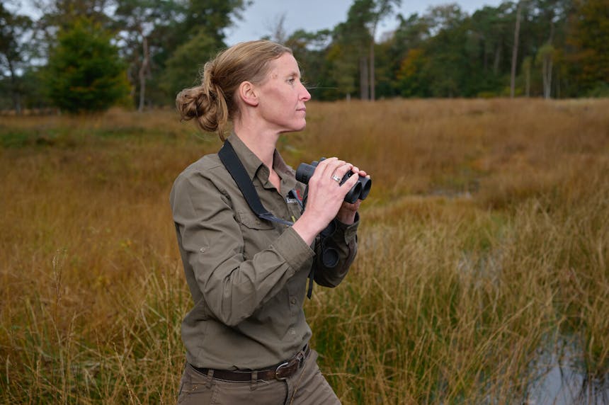 Medewerker van Geldersch landschap & Kasteelen met verrekijker staand in nat grasland op De Dellen en Heerder Sprengen.
