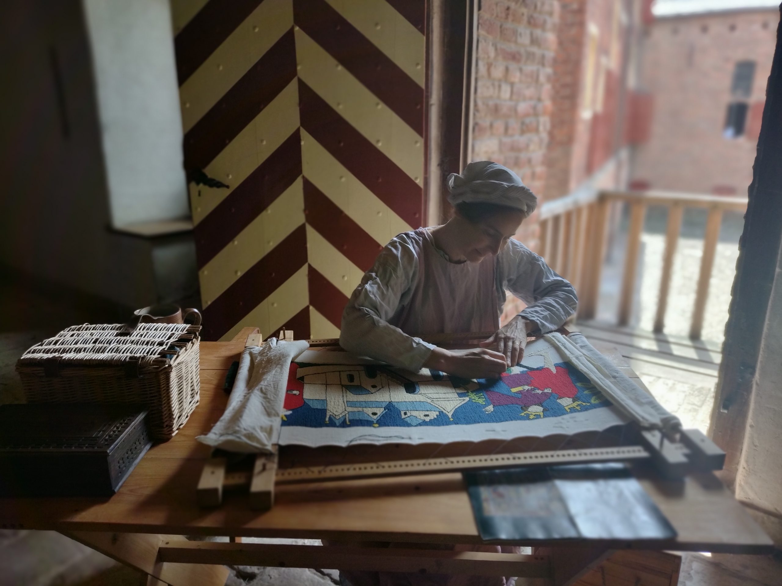 Historisch gekleede vrouw borduurt bij het open raam in kasteel Hernen
