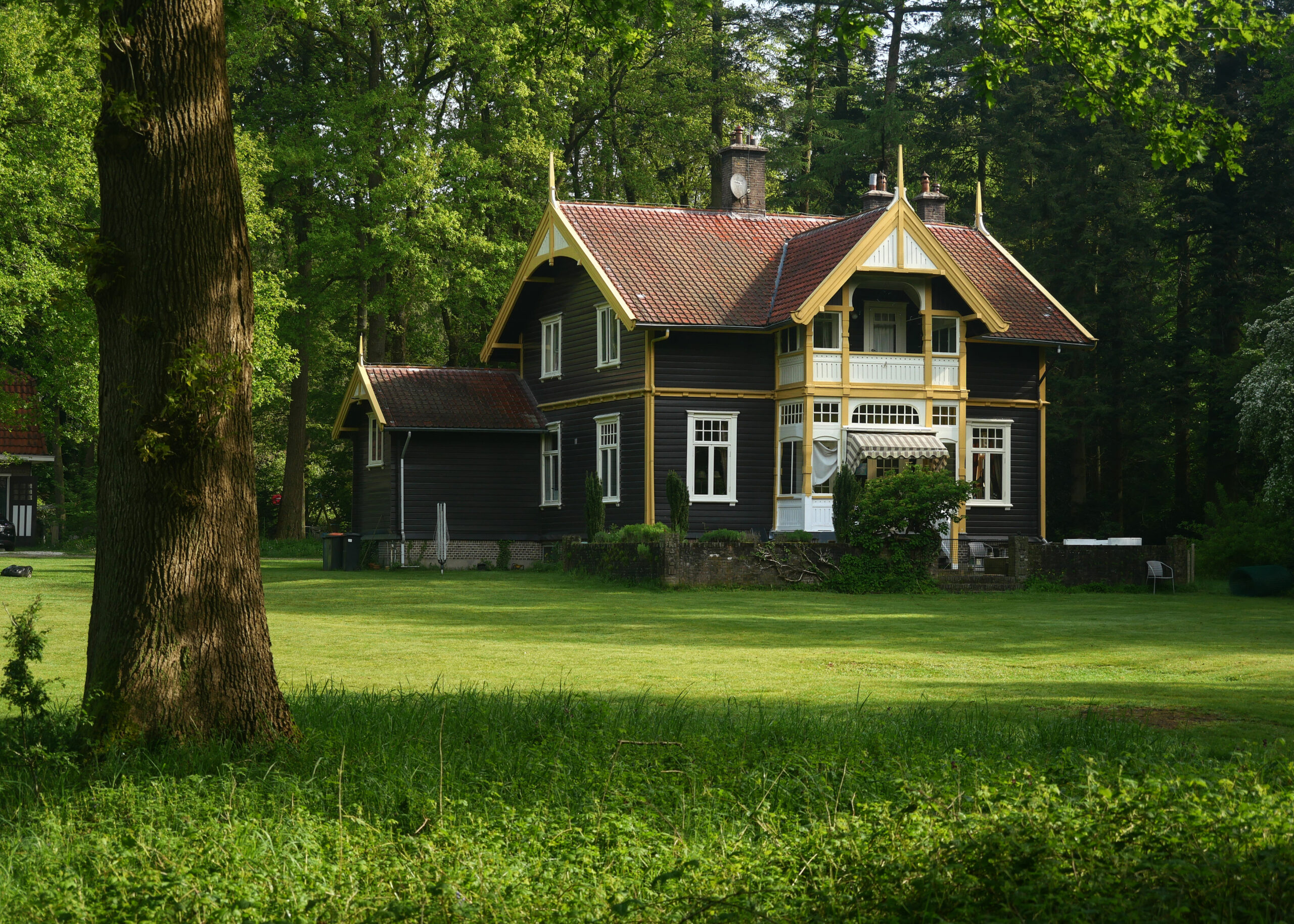 Noors houten huis omgeven door een groen gazon en hoge bomen in bosgebied Bruggelen.