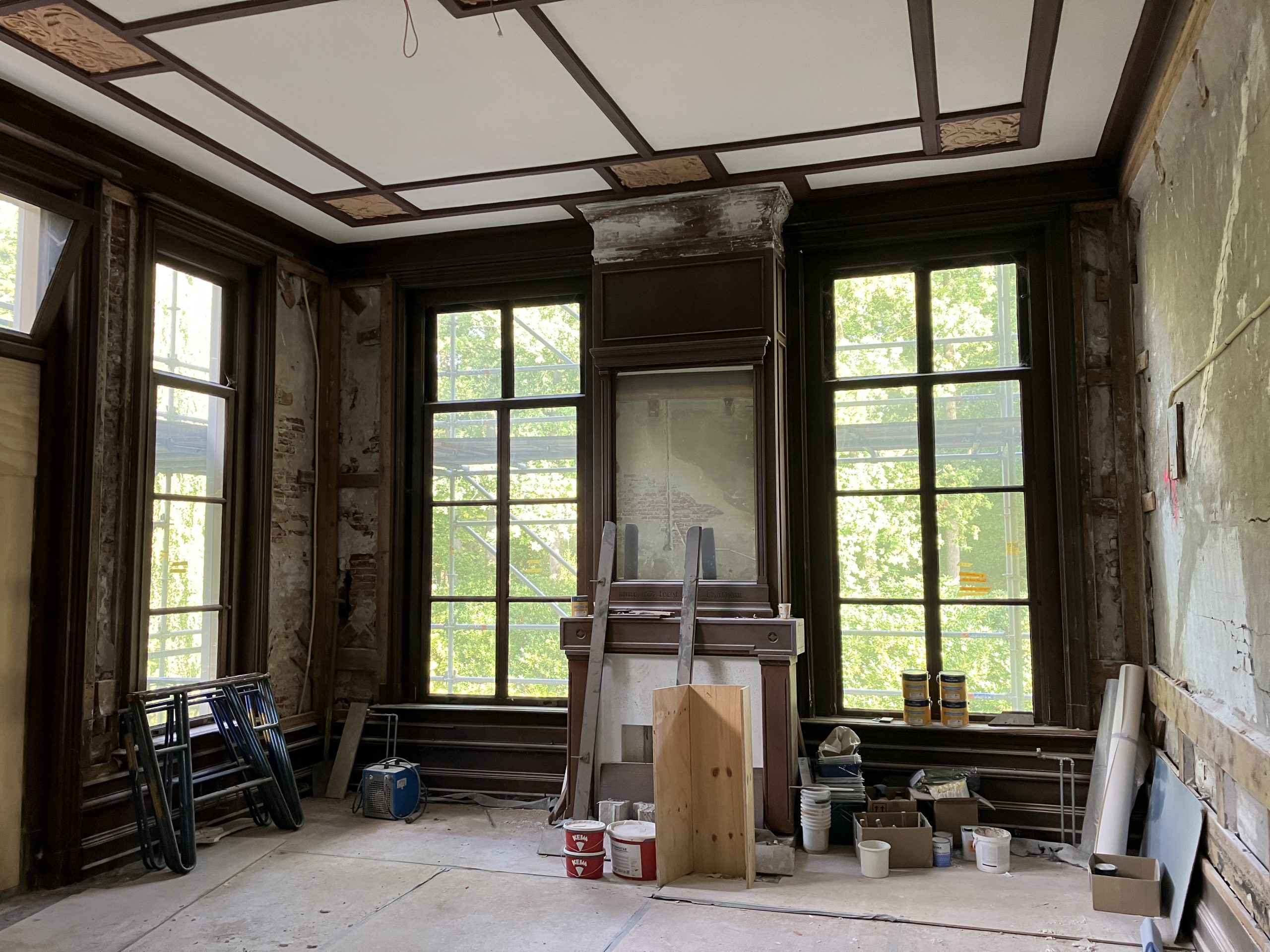 Restauratiewerkzaamheden aan schouw en muren in een kamer van kasteel Staverden, met door de ramen zicht op bouwsteigers.