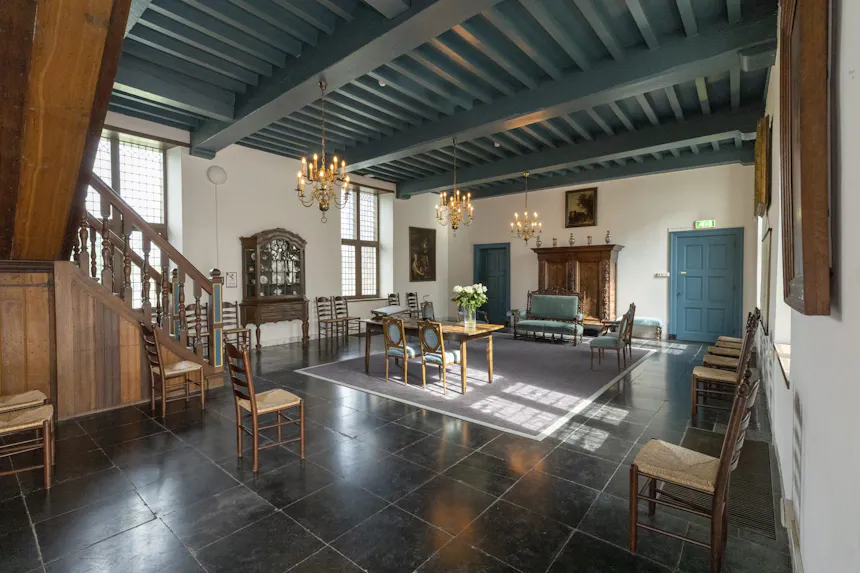 De trouwzaal in kasteel Ammersoyen, met een zwarte tegelvloer, een houten balkenplafond, kroonluchters, schilderijen aan de muren en antiek meubilair.