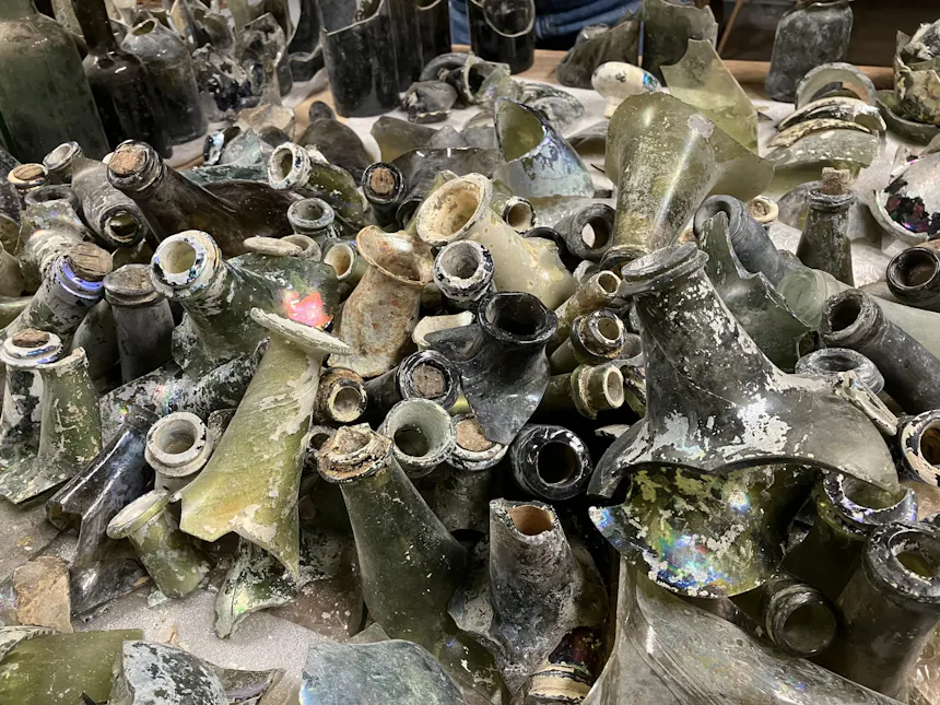 Op een tafel liggen eeuwenoude flessenhalzen, flessenbodems en scherven uitgestald; gevonden in de gracht van kasteel Ammersoyen.